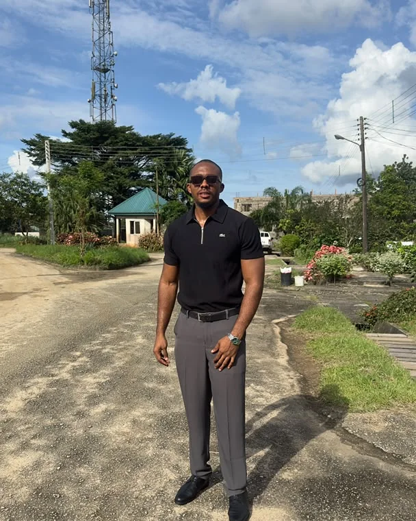 Emmanuel standing on a road in a black polo and sunglasses