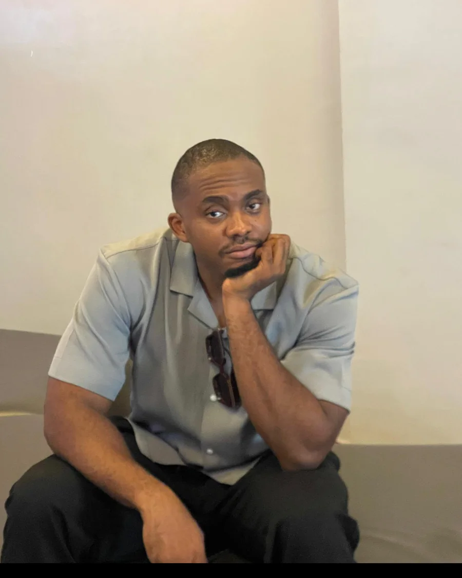 Emmanuel seated against a plain wall, chin resting on his hand